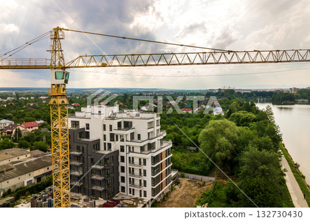 Aerial view of tower lifting crane and concrete frame of tall apartment residential building under construction in a city. Urban development and real estate growth concept. 132730430