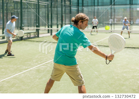 Padel game - man with partners plays on court 132730472
