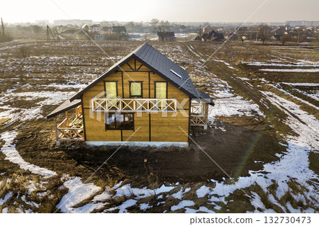 Aerial view of new wooden ecological traditional house cottage of natural lumber materials with steep shingle roof under construction on winter rural landscape background. Aerial view of new wooden ecological traditional house cottage of natural lumber materials with steep shingle roof under construction on winter rural landscape background. 132730473