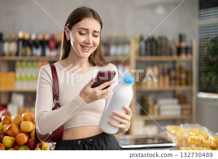 Female buyer checks suitability - scans QR code on bottle of milk label in grocery store Female buyer checks suitability - scans QR code on bottle of milk label in grocery store 132730489