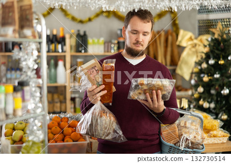 Young man choosing sweets for Christmas celebration in decorated shop 132730514