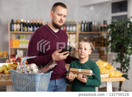 Man with phone and son choosing groceries Man with phone and son choosing groceries 132730528