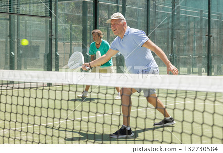 Mature man playing padel game in court on sunny day Mature man playing padel game in court on sunny day 132730584