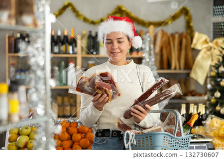 Female customer with a cart of groceries buys dried sausage and ham in supermarket - - prepares to celebrate Christmas Female customer with a cart of groceries buys dried sausage and ham in supermarket - - prepares to celebrate Christmas 132730607
