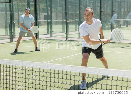 Padel game - man with partners plays on court 132730625