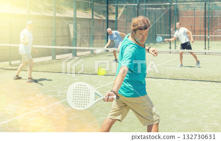 Four men practice playing padel on an outdoor court Four men practice playing padel on an outdoor court 132730631