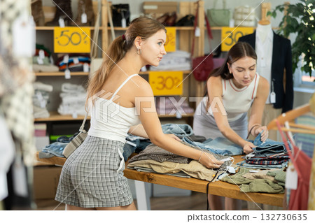 Young women customer making choice and elect trousers or shorts in store 132730635