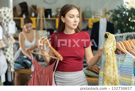 Young girl elect something summer clothing in store. Female client choosing something in background Young girl elect something summer clothing in store. Female client choosing something in background 132730657