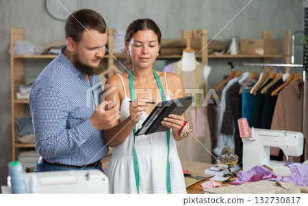 Female fashion designer creating custom clothing design with client in sewing studio Female fashion designer creating custom clothing design with client in sewing studio 132730817