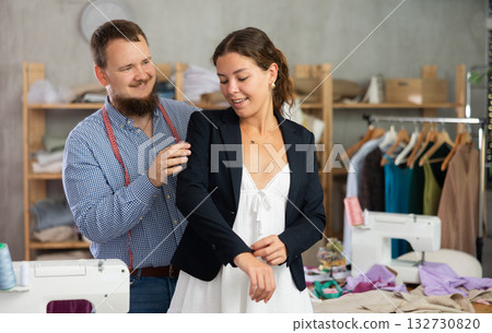 Female client trying on custom blazer with tailor in workshop Female client trying on custom blazer with tailor in workshop 132730820