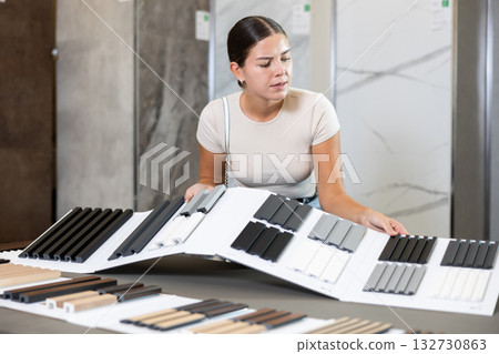 Woman chooses decorative wall or floor coverings for her home with interest 132730863