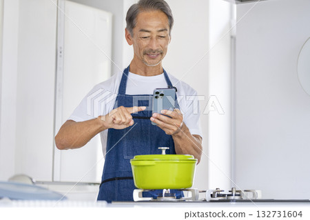 Senior man operating a smartphone while cooking Senior man operating a smartphone while cooking 132731604