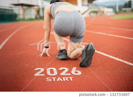 Athletic Female Runner Preparing to Start Race on Track Marked 2026, Signifying Future Competitions and Goals in Sports and Fitness 132731607