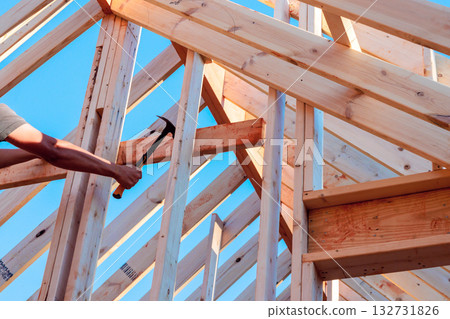 Skilled worker uses hammer to secure wooden beams in construction project Skilled worker uses hammer to secure wooden beams in construction project 132731826