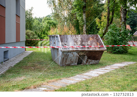 Rusty metal waste container placed near a building and surrounded by red and white safety tape Rusty metal waste container placed near a building and surrounded by red and white safety tape 132732813