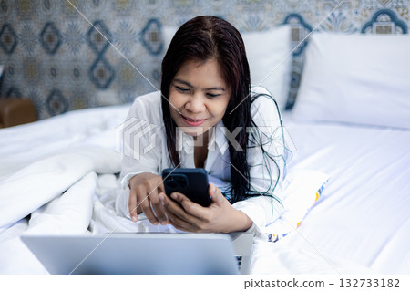 Asian woman using smartphone and laptop on bed at home, relaxing lifestyle and online communication Asian woman using smartphone and laptop on bed at home, relaxing lifestyle and online communication 132733182
