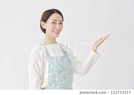 一位身穿圍裙的女子，在白色背景下用手掌指向右側。 132733217