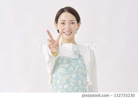 Woman wearing an apron making a peace sign on a white background 132733230