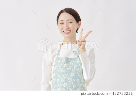 Woman wearing an apron making a peace sign on a white background 132733231