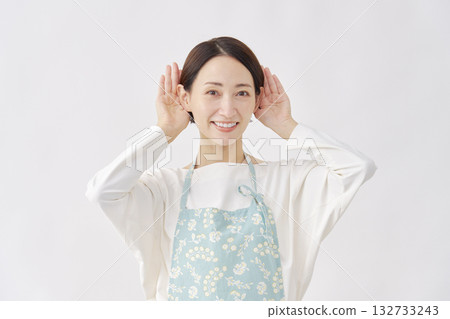 Woman wearing an apron making a listening gesture on a white background 132733243