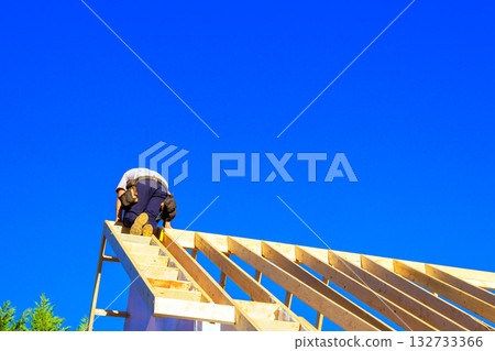 Worker is installing adding wooden rafters to roof under construction of wooden framed 132733366