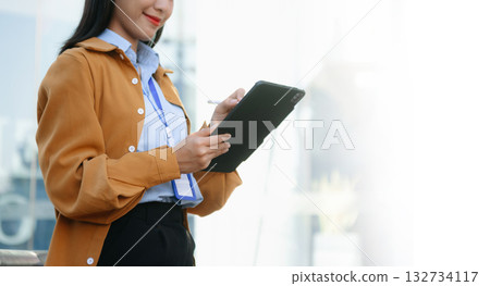 Confident Asian businesswoman smiling while using a smartphone outdoors, symbolizing technology, success, and modern professional lifestyle. 132734117