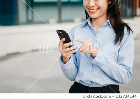 Asian woman with a smile standing holding notepad and tablet at out side office. big city on business center background. 132734144
