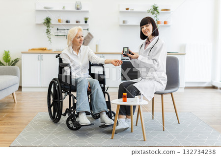 A doctor is checking the blood glucose level of a senior woman in a wheelchair at home. The doctor is holding a blood glucose meter. A doctor is checking the blood glucose level of a senior woman in a wheelchair at home. The doctor is holding a blood glucose meter. 132734238