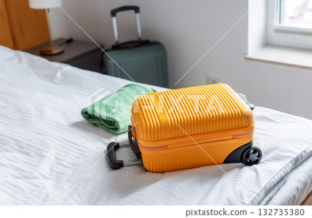 Orange suitcase and folded clothes resting on hotel bed 132735380