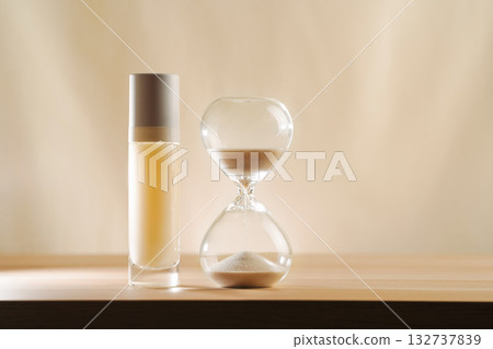 A modern still life featuring skincare product with an hourglass, embodying timeless beauty and minimalism. A focus on creativity and elegance in self-care displayed on a serene, neutral backdrop. 132737839