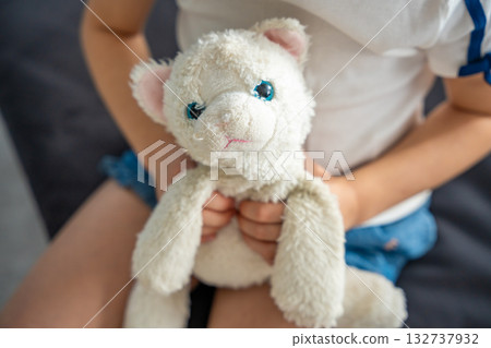 Child holding a well-worn plush toy tightly in both hands. Emotional connection to a beloved object that provides comfort, security, and a sense of familiarity in early childhood. Child holding a well-worn plush toy tightly in both hands. Emotional connection to a beloved object that provides comfort, security, and a sense of familiarity in early childhood. 132737932