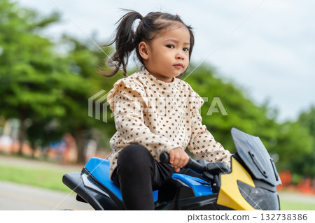 toddler girl riding an electric motorcycle toy in park toddler girl riding an electric motorcycle toy in park 132738386