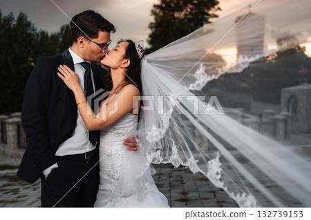 Interracial wedding couple kissing outdoors with flowing veil 132739153