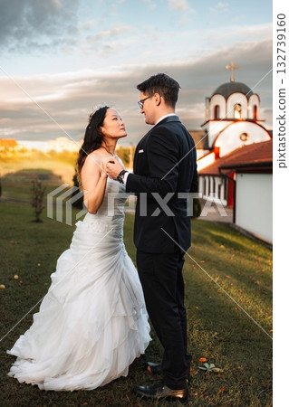 Interracial wedding couple looking at each other by church at sunset Interracial wedding couple looking at each other by church at sunset 132739160
