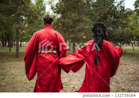 Couple in traditional Chinese wedding outfits walking together in a park Couple in traditional Chinese wedding outfits walking together in a park 132739164