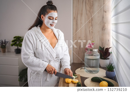 Young Woman with Face Mask Preparing Detox Water with Lemon and Cucumber in the Kitchen Young Woman with Face Mask Preparing Detox Water with Lemon and Cucumber in the Kitchen 132739210