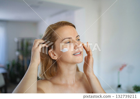 Mid adult woman applying face cream at home Mid adult woman applying face cream at home 132739211