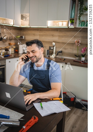 Handyman working on laptop and talking on phone in kitchen Handyman working on laptop and talking on phone in kitchen 132739285