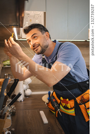 Electrician installing led strip lights under kitchen cabinets Electrician installing led strip lights under kitchen cabinets 132739287