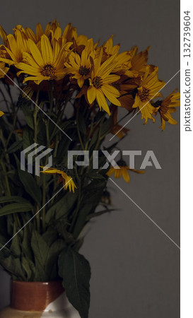 Rustic arrangement of bright yellow wildflowers placed in a ceramic vase, set against a plain indoor wall. Rustic arrangement of bright yellow wildflowers placed in a ceramic vase, set against a plain indoor wall. 132739604
