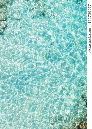 Clear turquoise waters ripple gently over rocky seabed in a tropical paradise, inviting visitors to explore underwater wonders under bright sunlight 132739977