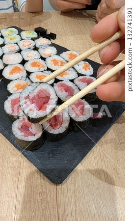 Enjoy some delicious and colorful sushi rolls served with chopsticks on a beautiful slate board 132741391