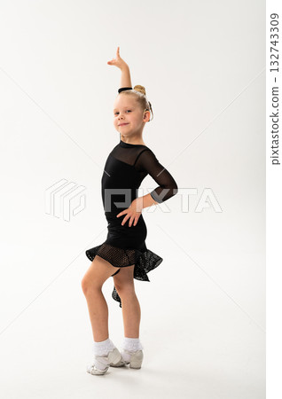 Little girl in black latin dance dress performing graceful pose with cochlear implant. Overcoming hearing loss through movement, inclusion, and confidence in art and rhythmic self-expression. 132743309