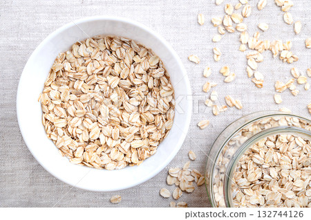 Rolled oats, thick-rolled and old-fashioned oats, in a white bowl, on linen. Dehusked and steamed oat groats, rolled into flakes under heavy rollers, then stabilized by being lightly toasted. Photo Rolled oats, thick-rolled and old-fashioned oats, in a white bowl, on linen. Dehusked and steamed oat groats, rolled into flakes under heavy rollers, then stabilized by being lightly toasted. Photo 132744126