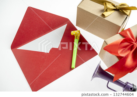 Top view of red envelope or postcard and gift box with plastic horn and party blowers on white background. Mockup, blank template, copy space. Greeting or invitation card with flat lay style 132744604