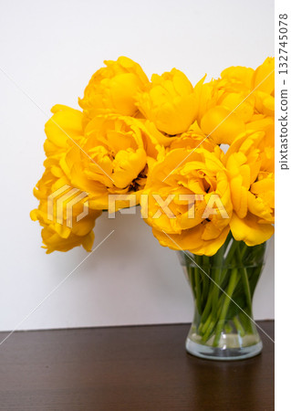 A boy stands indoors holding a large bouquet of yellow tulips, radiating happiness with a big smile on his face. Mother's Day and spring concept. A boy stands indoors holding a large bouquet of yellow tulips, radiating happiness with a big smile on his face. Mother's Day and spring concept. 132745078