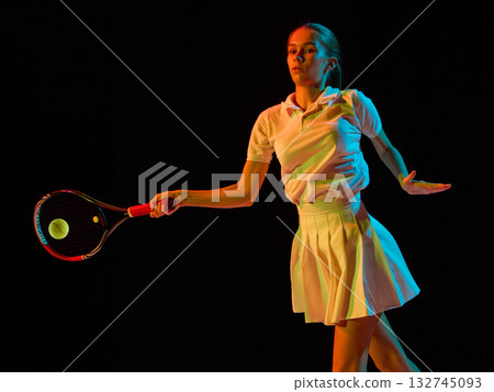 Female tennis player hitting ball in focused forehand motion under colored light 132745093