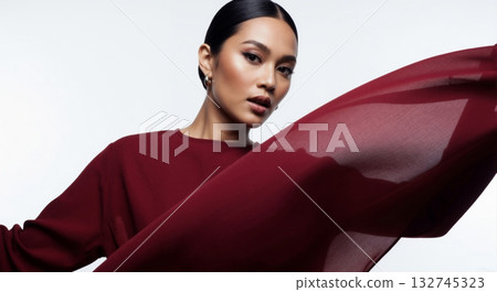 Confident fashion model with slicked back hair and makeup. Dynamic portrait with flowing red fabric on a white background Confident fashion model with slicked back hair and makeup. Dynamic portrait with flowing red fabric on a white background 132745323