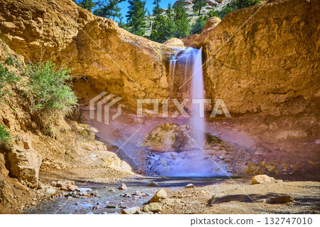 Waterfall Flowing Over Sandstone Cliffs with Stream and Greenery in Natural Sunlight Waterfall Flowing Over Sandstone Cliffs with Stream and Greenery in Natural Sunlight 132747010