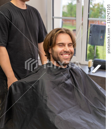 A happy man with a beard and closed eyes sits in a barbershop chair, 132747105